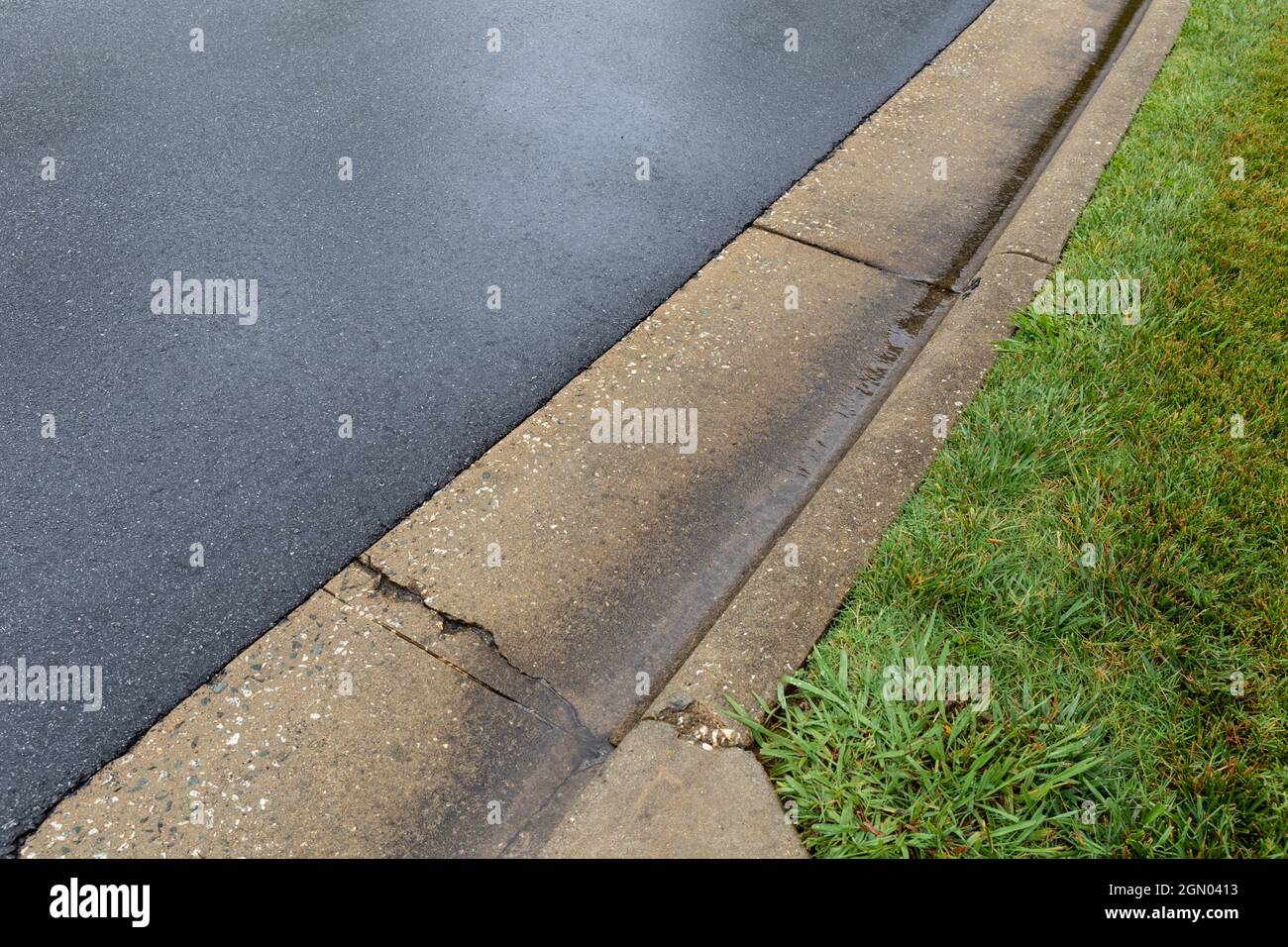 Diagonale Ansicht einer nassen Asphaltstraße, die in eine geformte Betonkanone mit grasbewachsenen Landschaftsgestaltung abfliesst, Transport-Thema mit kreativem Kopierraum, ho Stockfoto