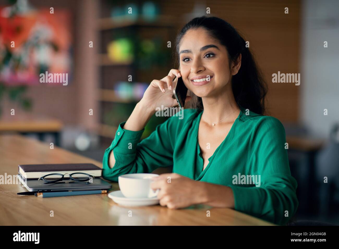 Lächelnde Brünette indische Frau trinkt Kaffee, Telefongespräch Stockfoto