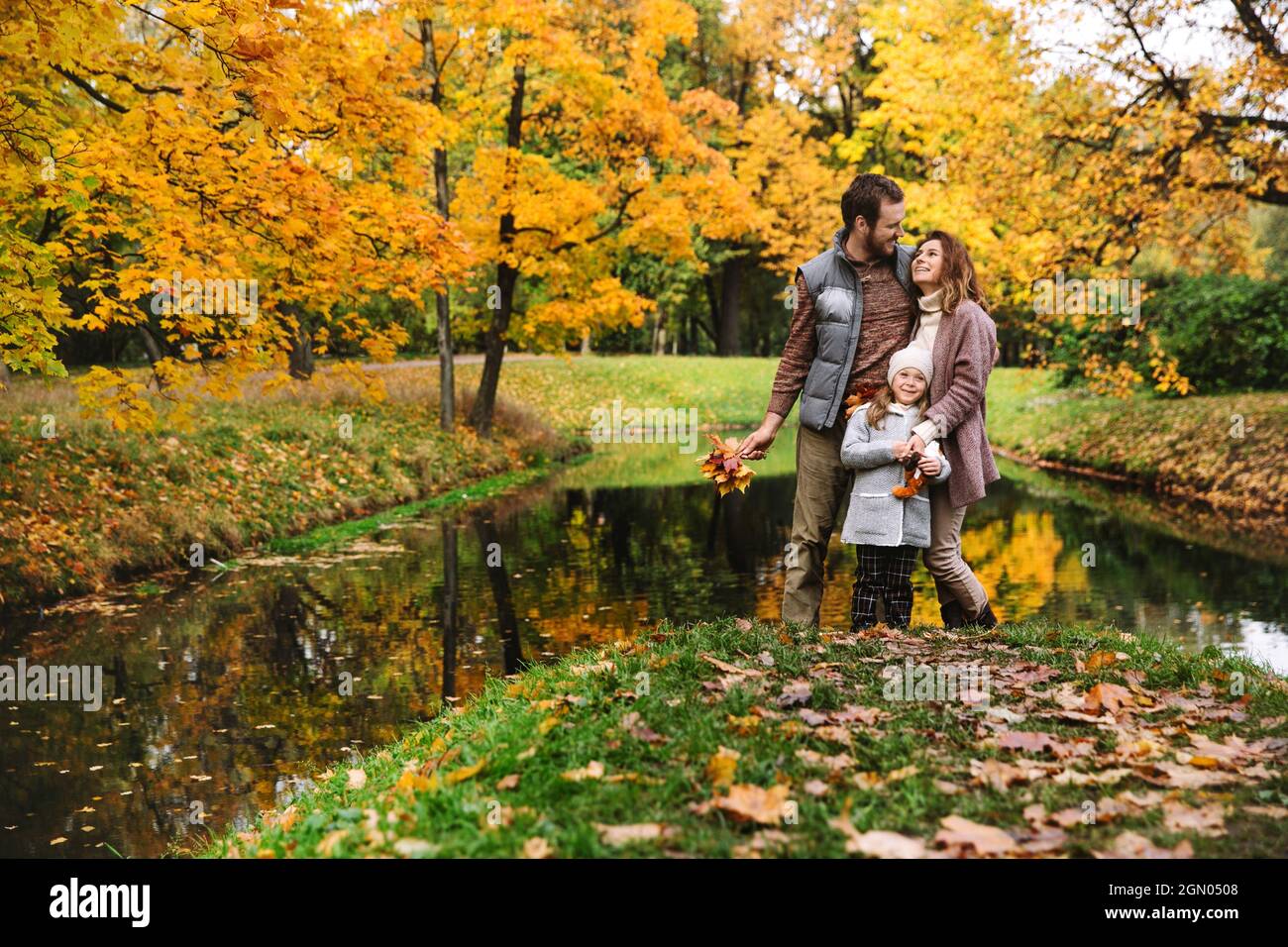 Liebevolle Familie von drei im Herbstwald: Eltern und Kind Tochter umarmen auf entspannenden Spaziergang im Park Stockfoto