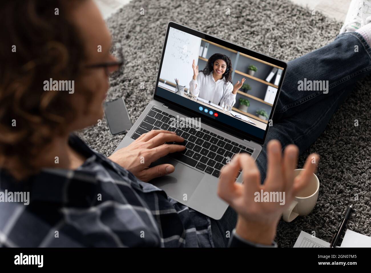 Millennial Mann sehen Online-Lektion, grüßt Lehrer und zeigt ok Schild mit der Hand zu Hause. afroamerikanische Tutorin ruft auf dem Laptop-Bildschirm an. Neu Stockfoto