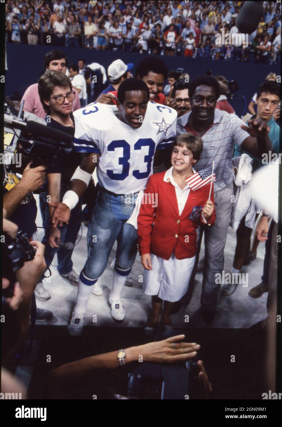 Dallas Texas USA, 1984: Die olympische Goldmedaillengewinnerin Mary Lou Retton, die während der Sommerspiele 1984 in Los Angeles für ihre Olympia-Heldinnen geehrt wurde, posiert mit Dallas Cowboys, die vor einem Cowboys-Spiel Tony Dorsett im Texas Stadium zurücklaufen. ©Bob Daemmrich Stockfoto