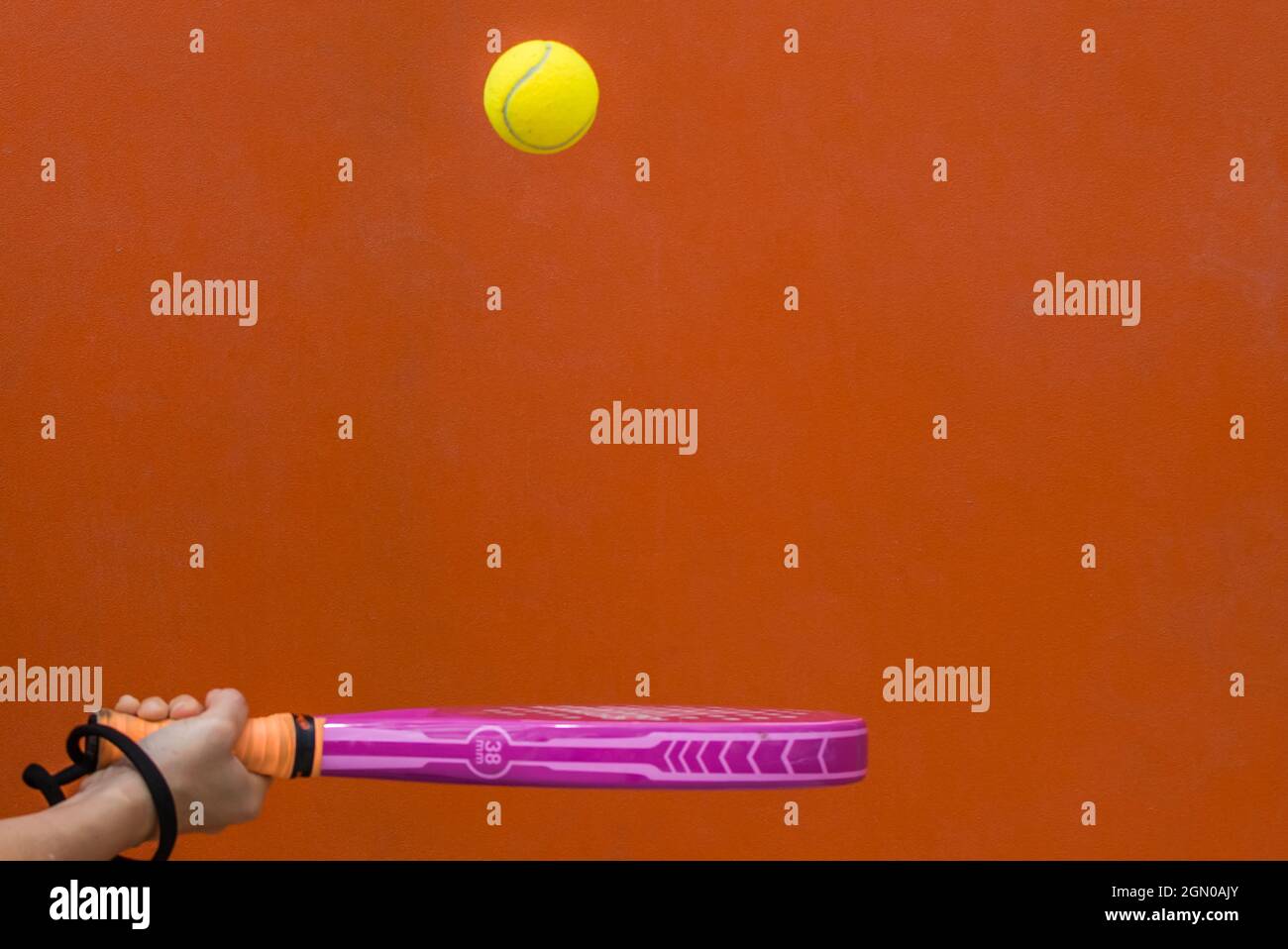 Hand hält Einen Paddle Tennis Racket und schlägt den Ball auf einem orangefarbenen Hintergrund.Sport Stockfoto