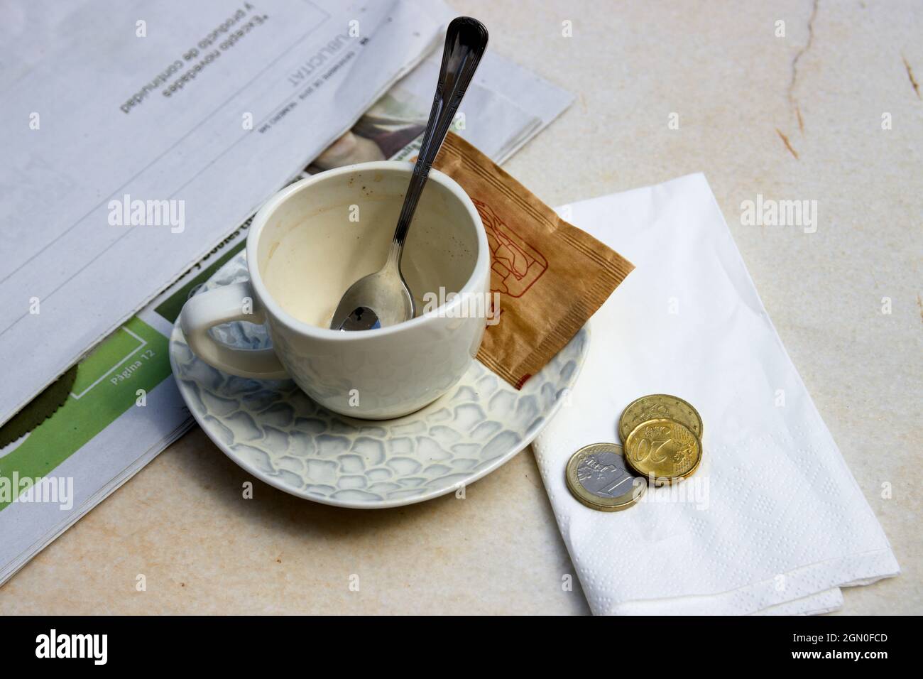 Nahaufnahme einer Tasse Kaffee oder Tee in einer Bar, daneben eine Zeitung und einige Münzen mit dem Getränkepreis oder dem Trinkgeld für die Kellner Stockfoto