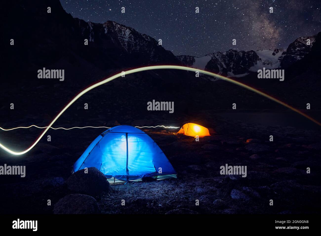 Blau-gelbes Gloving-Zelt mit Lichtlinie beim Campen in den Bergen unter Nachthimmel mit Sternen Stockfoto