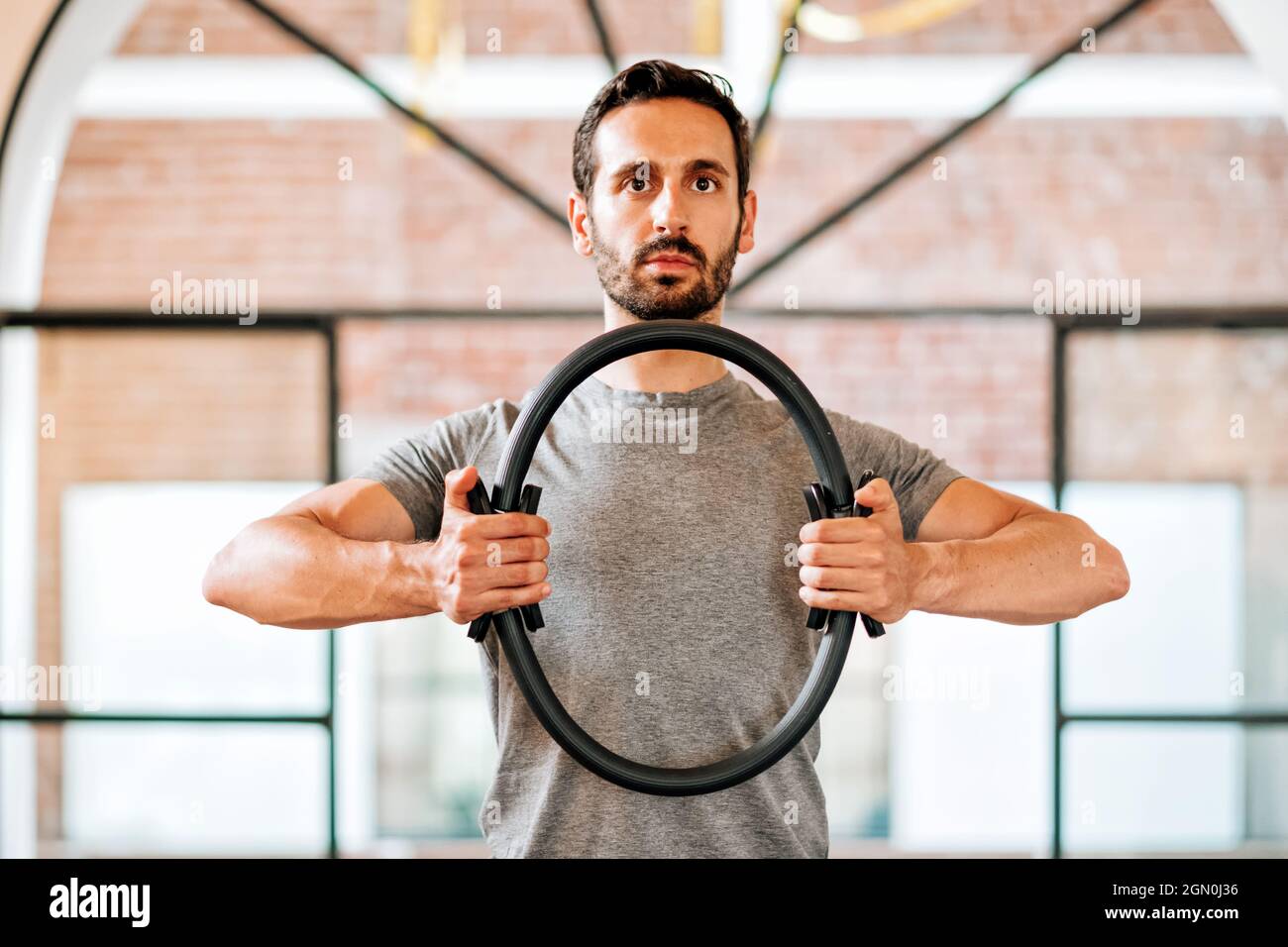 Passen Sie den athletischen Mann mit einem Pilates Magic Circle oder Ring an, um seine Muskeln zu stärken und seine Haltung in einem Fitnessstudio in einer Nahaufnahme des Oberkörpers auszurichten Stockfoto