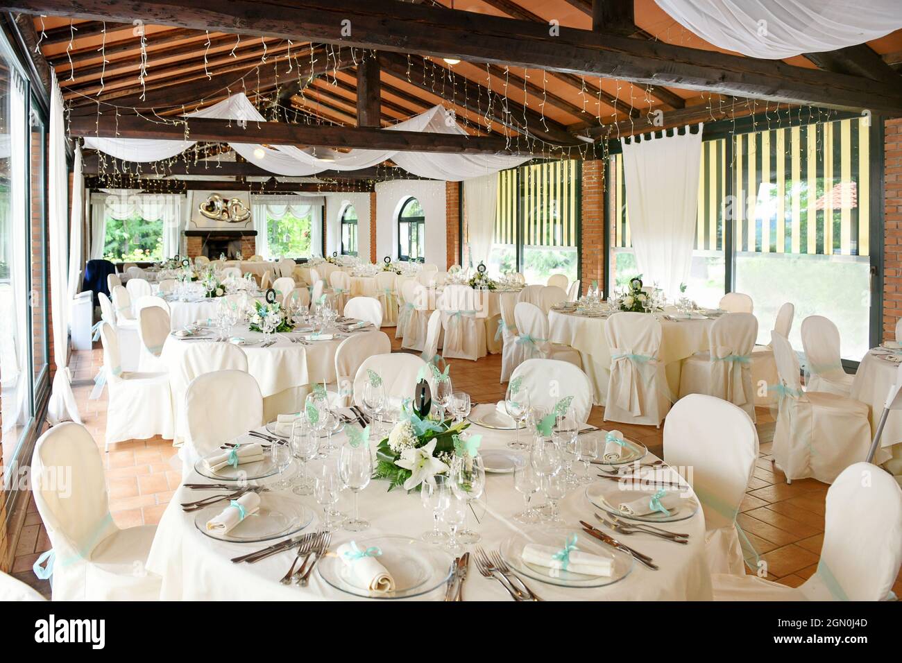 Elegantes Innendesign des Restaurants mit runden Tischen mit Geschirr und Blumen in zarten Weiß- und Blautönen, serviert für festliche Hochzeitsempfänge Stockfoto
