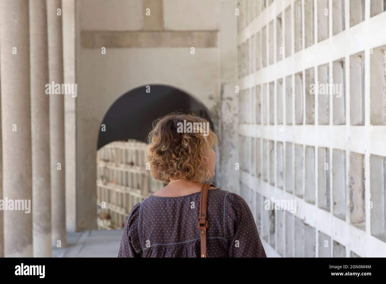 Unbekannte Frau mit lockigen blonden Haaren und dem Rücken gedreht, auf der Suche nach dem Grab eines Verwandten in mehreren Reihen von Nischen, Tag der Toten Konzept. Stockfoto