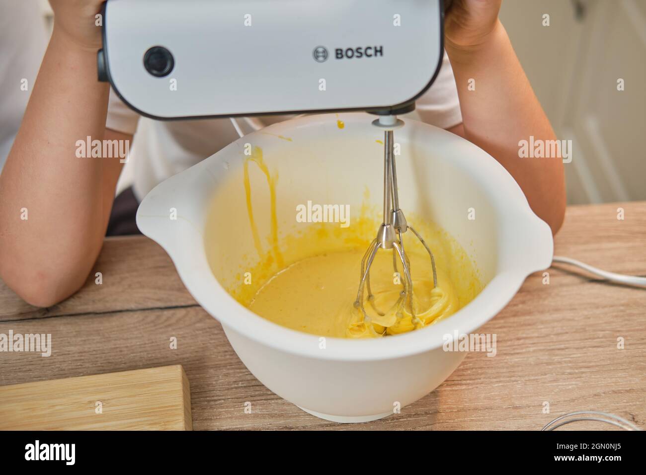 Junge in weißer Chefkleidung schlägt Eier mit einem Bosch-Mixer, um in seiner eigenen Küche einen Kuchen zu backen - Moskau, Russland, 2. September 2021 Stockfoto