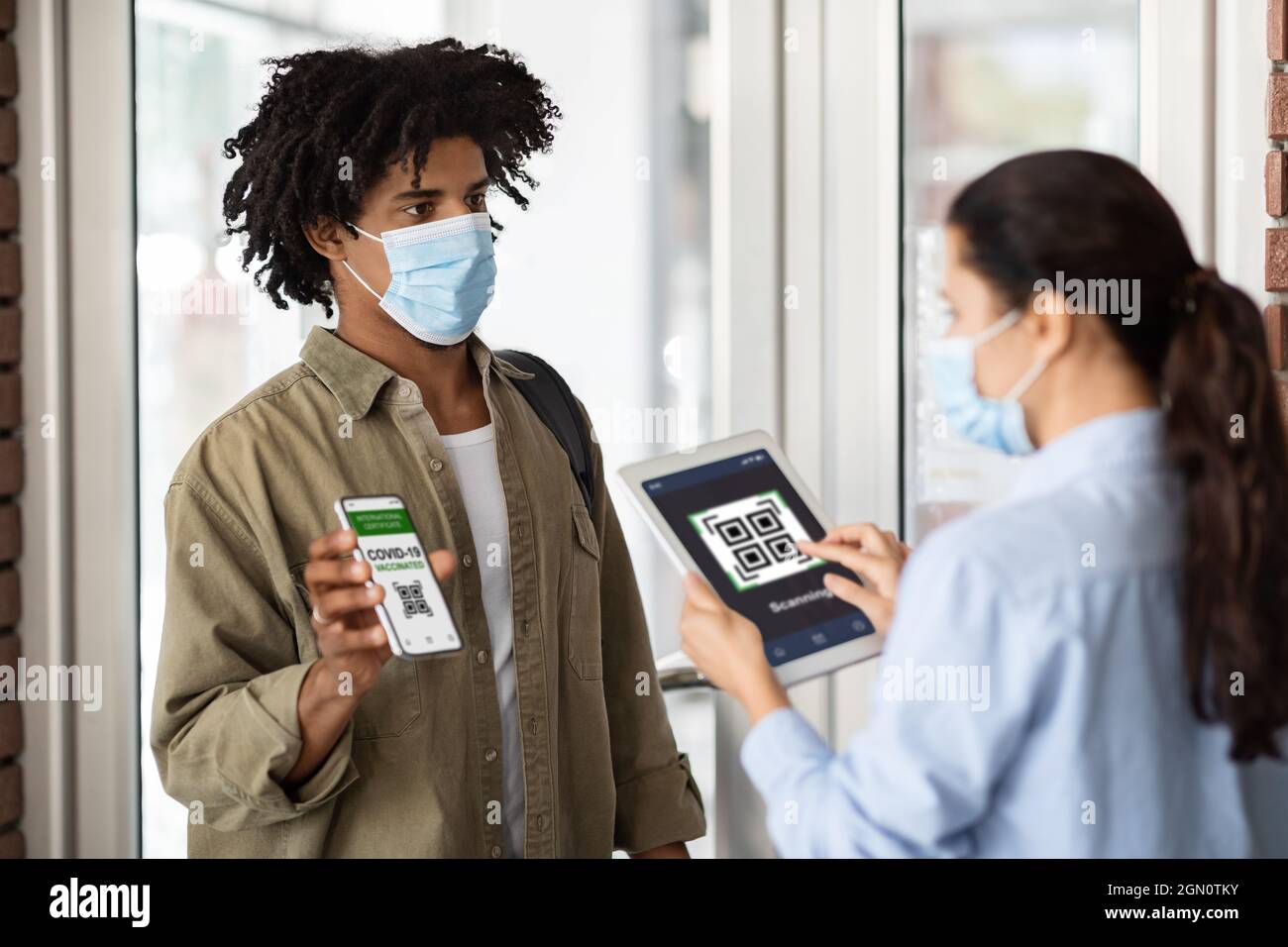 Junger Afroamerikanischer Mann Mit Impfpass Auf Dem Smartphone Am Eingang Des Cafés Stockfoto