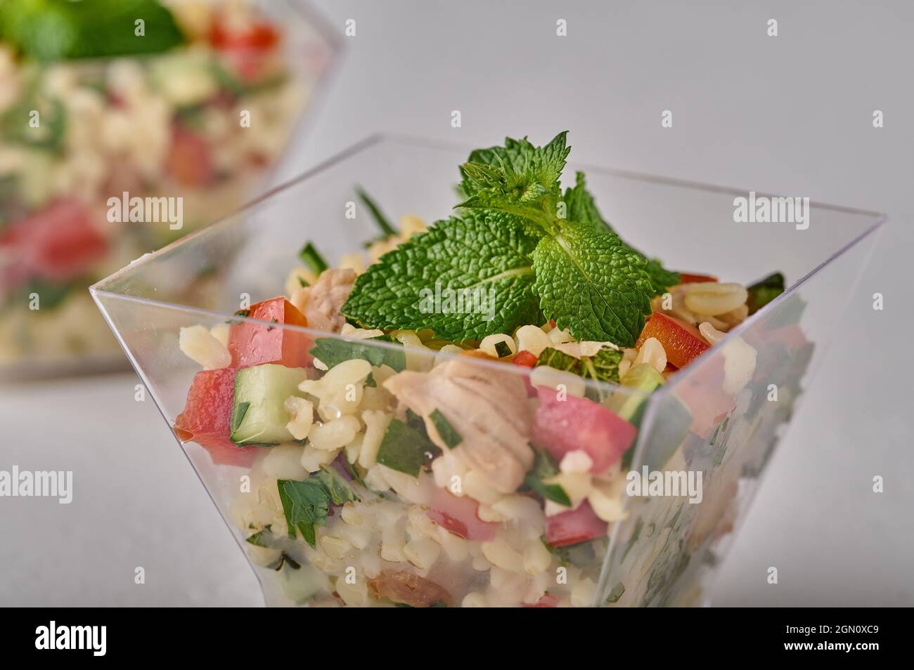 Macro Tabbouleh Salat mit Petersilie, Minze, Bulgur, Tomaten in transparenter Buffetform auf weißem Hintergrund. Selektiver Fokus Stockfoto