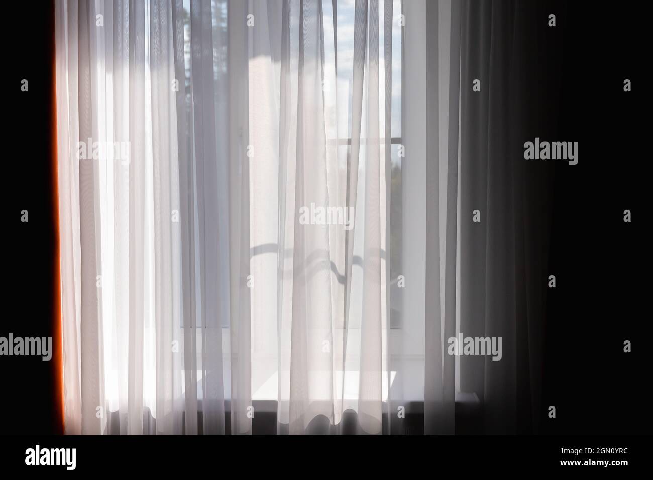 Welliger weißer Tüll vor dem hellen Fenster an einem sonnigen Tag. Hintergrundbild Stockfoto