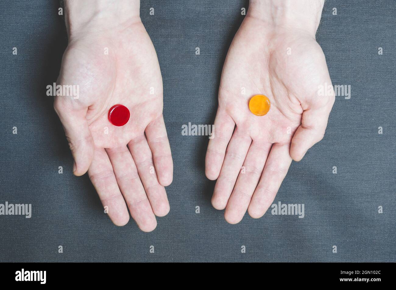 Zwei Tabletten rot und gelb in verschiedenen Händen, Wahl. Stockfoto