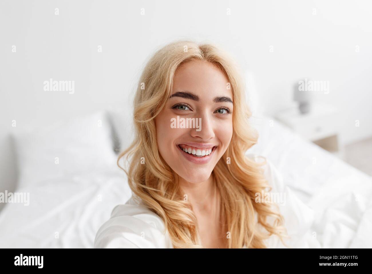 Lächelnde, tausendjährige europäische blonde Dame im Bademantel genießt den guten Morgen und macht Selfie Stockfoto