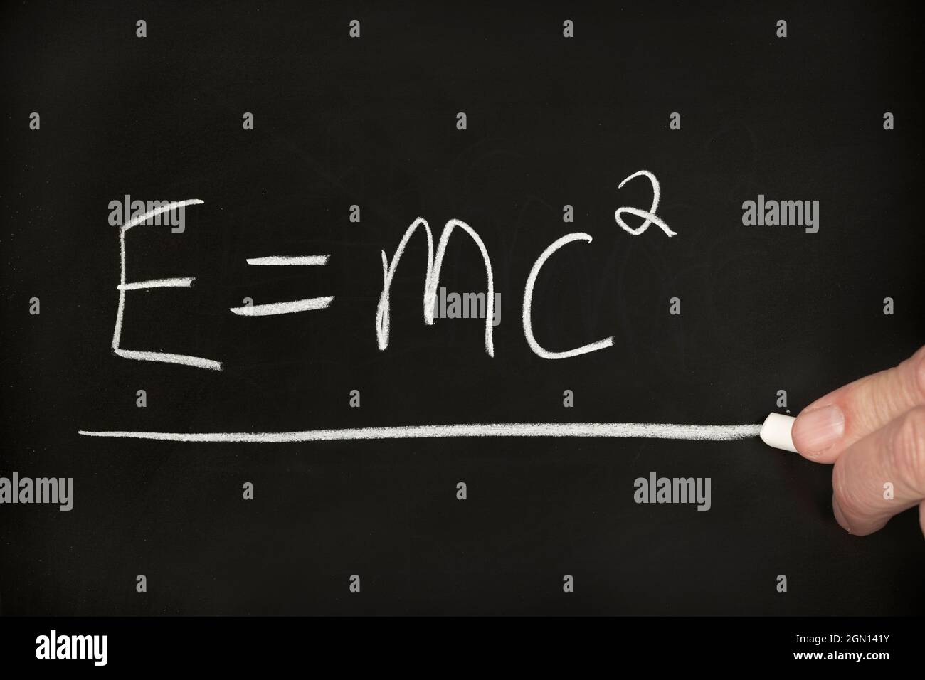 Ein Lehrer schreibt die Relativitätstheorie der Einstein-Gleichung auf einem schwarzen Schwarzen Brett, während er eine Gruppe von Schülern in einem Klassenzimmer unterrichtet. Stockfoto