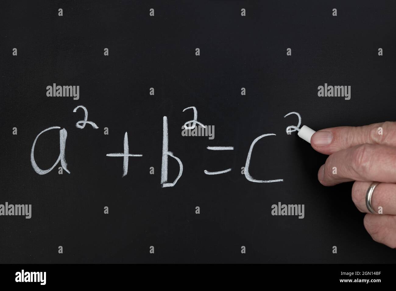 Ein Lehrer schreibt die Pythagoräische Theoremgleichung auf einer schwarzen Tafel, während er eine Gruppe von Schülern in einem Klassenzimmer unterrichtet. Stockfoto