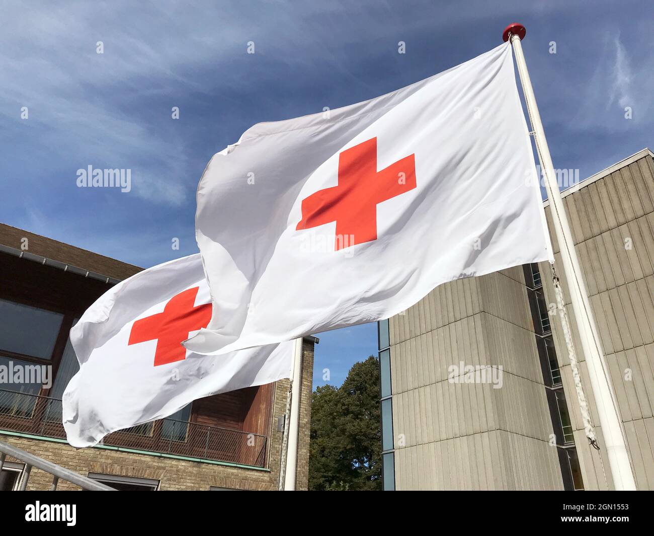 Two Red Cross flags waving in the wind against a blue sky. Close up photo. Copenhagen, Denmark - September 4, 2021. Stockfoto