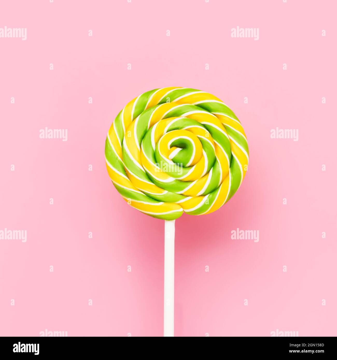 Gelb-grüner Lollipop wirbelt auf einem weißen Stock über rosa Hintergrund. Draufsicht, Platz für Text kopieren Stockfoto