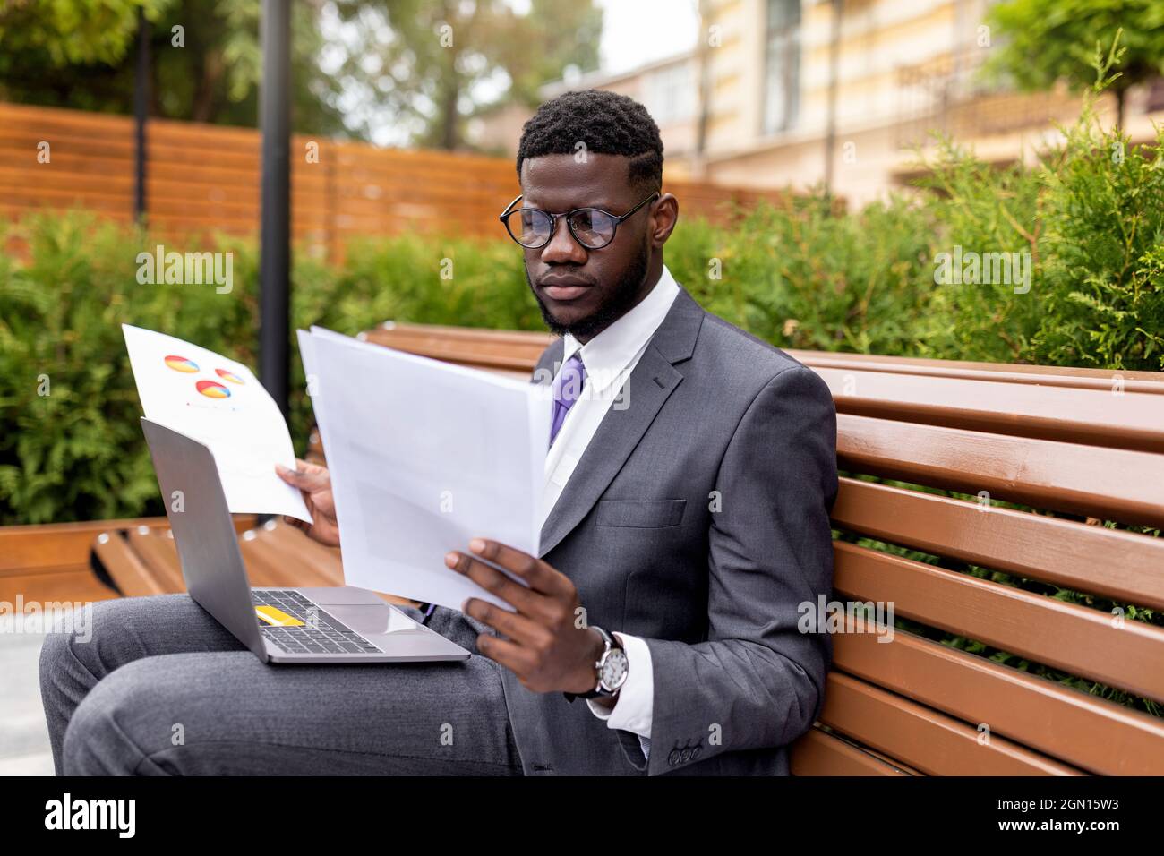 Konzentrierter afroamerikanischer Unternehmer sitzt im Büro mit Laptop und liest Dokumente, freier Platz Stockfoto