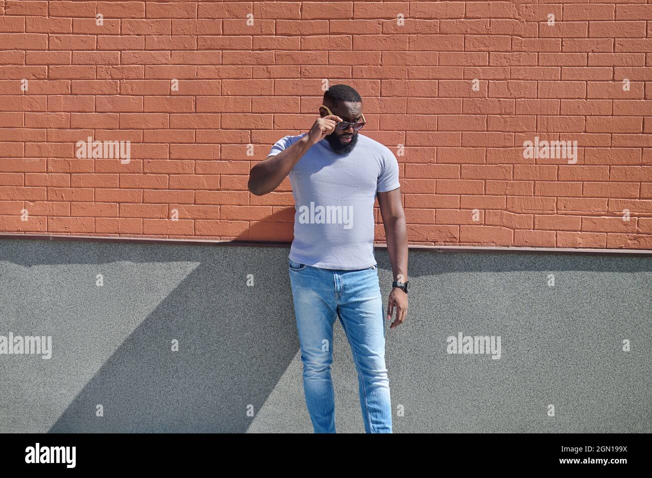 Ein dunkelhäutiger Mann in einem weißen T-Shirt und Jeans in der Nähe der Backsteinmauer Stockfoto