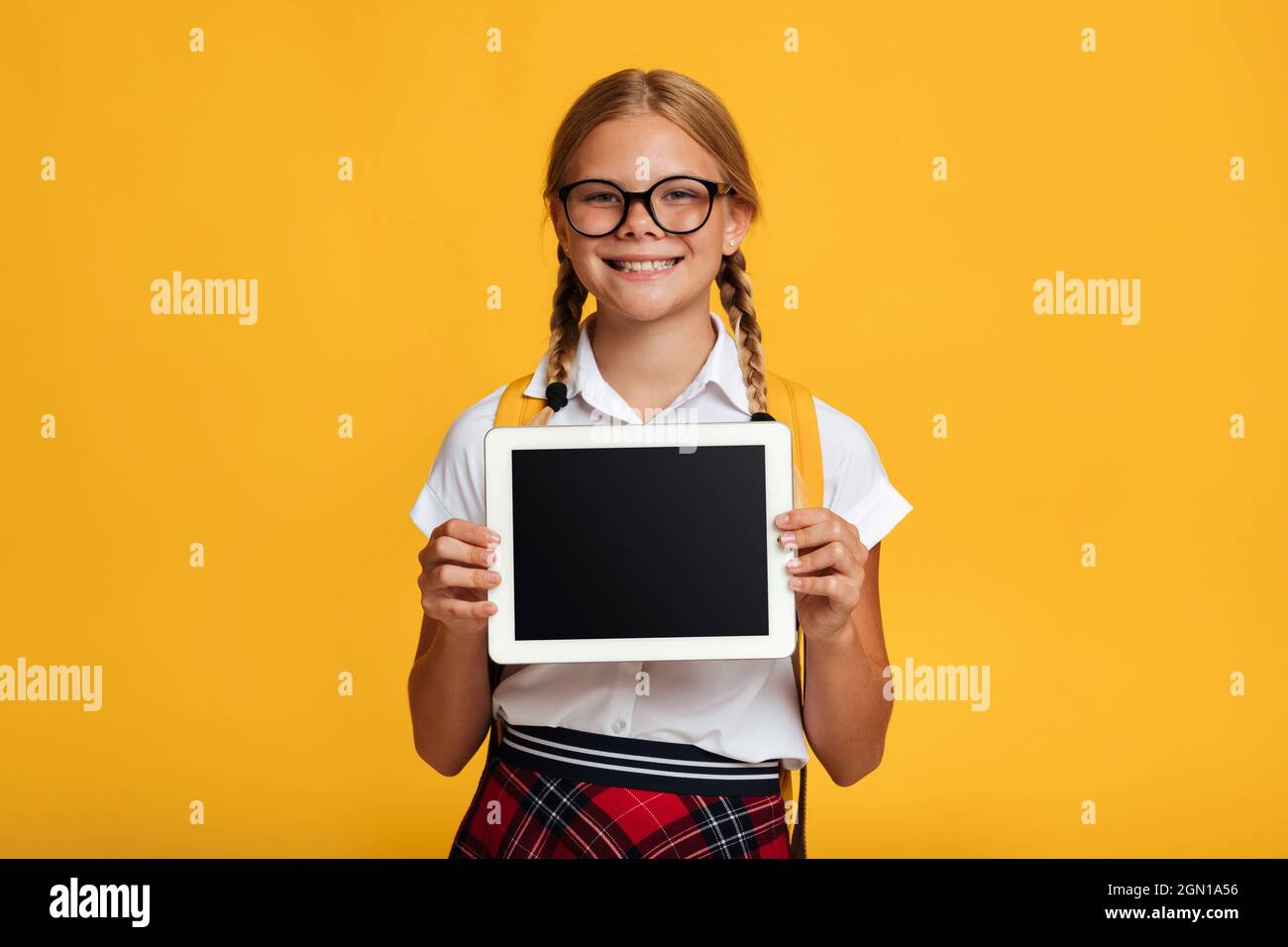 Frohes Jugendalter blondes Schulmädchen in Brille zeigt Tablet mit leerem Bildschirm Stockfoto