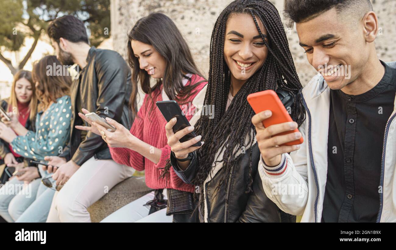 Eine Gruppe von Freunden, die mit ihren Smartphones im Freien spielen – fröhliche junge Menschen, die im Freien mit dem Handy telefonieren. Technisches Konzept. Stockfoto