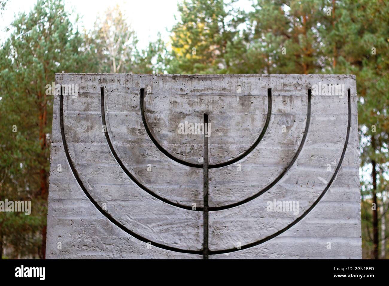 Defokussieren Sie das Menorah-Symbol auf Betonplatten in Wald und Natur. Symbole des jüdischen Volkes. Erinnerung und Ehrfurcht.außer Fokus Stockfoto
