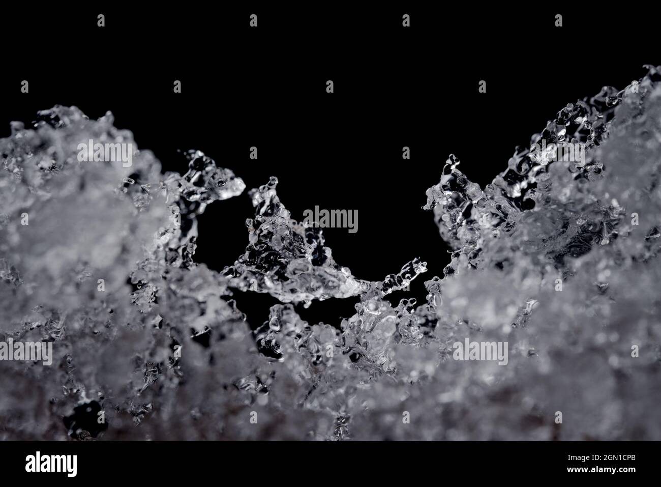 Komplizierte Details von schmelzenden Wasserpartikeln. Konzentrieren Sie sich auf einen seltsam geformten Eiskristall in der Mitte, aber auf einen schlichten schwarzen Hintergrund mit Kopierbereich oben. Stockfoto