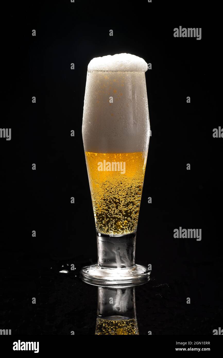 Eine Nahaufnahme uof ein Glas Bier vor schwarzem Hintergrund beginnt zu überlaufen. Stockfoto