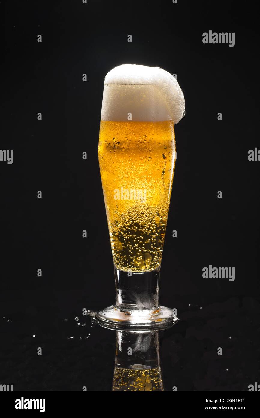 Eine Nahaufnahme uof ein Glas Bier vor schwarzem Hintergrund beginnt zu überlaufen. Stockfoto