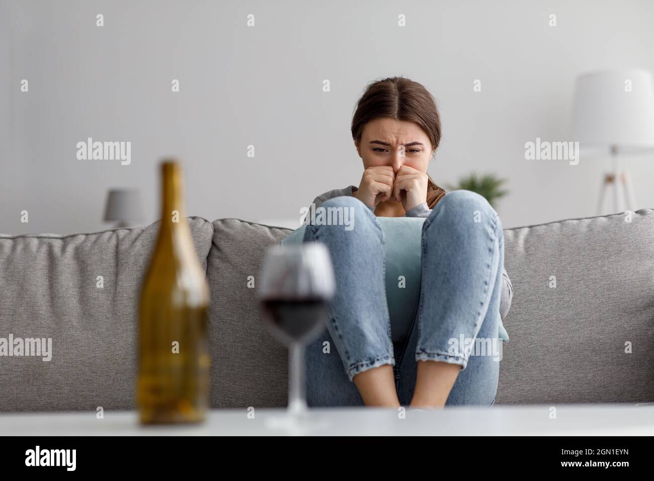 Trauriges Weinen verzweifelte junge europäische Dame, die unter Stress, Trauer und Schwierigkeiten mit Flasche und Glas Wein litt Stockfoto