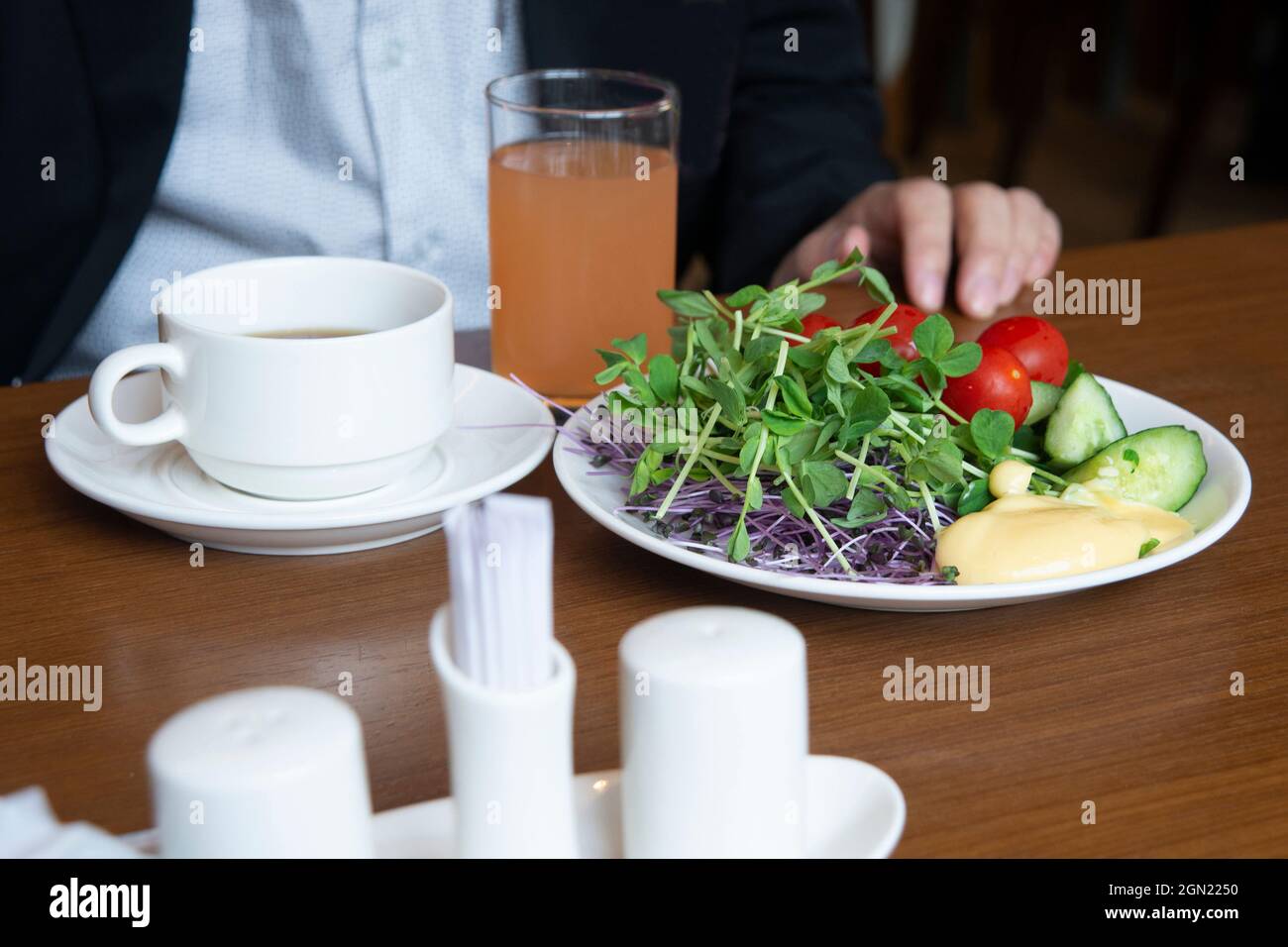 Nur ein Mann sitzt am Esstisch und serviert ein gesundes Frühstück mit Orangensaft und heißem Tee. Stockfoto