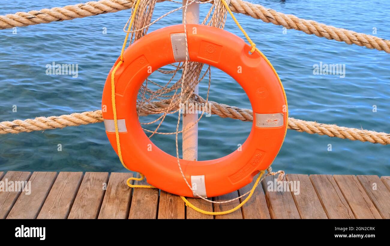 Orangefarbene Rettungsleine und Meerseile auf dem Hintergrund des Meeres und des blauen Himmels. An einem Pfosten hängen Meeresschnüre und Rettungsmittel. Hilfe- und Sicherheitskonzept Stockfoto