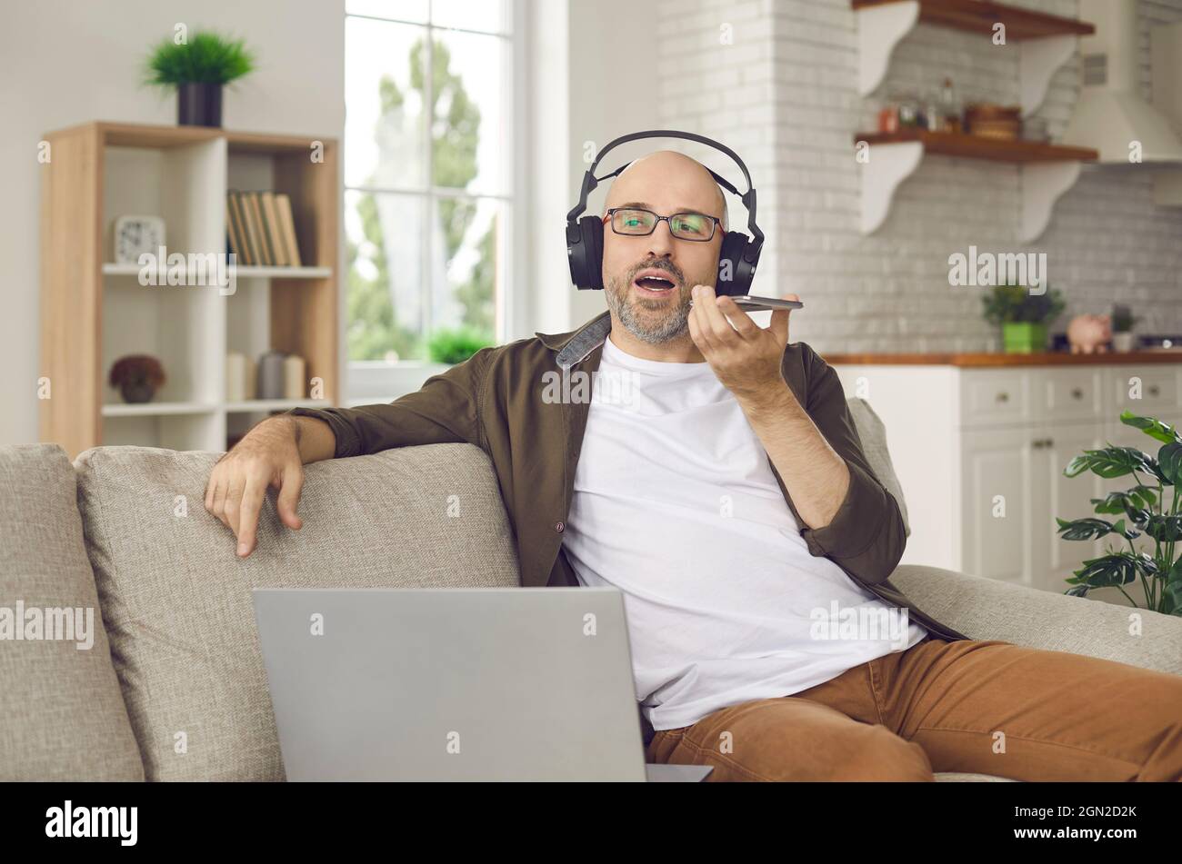 Mann, der Voicemail aufzeichnet oder auf einem Freisprechtelefon spricht, während er zu Hause auf dem Sofa sitzt Stockfoto