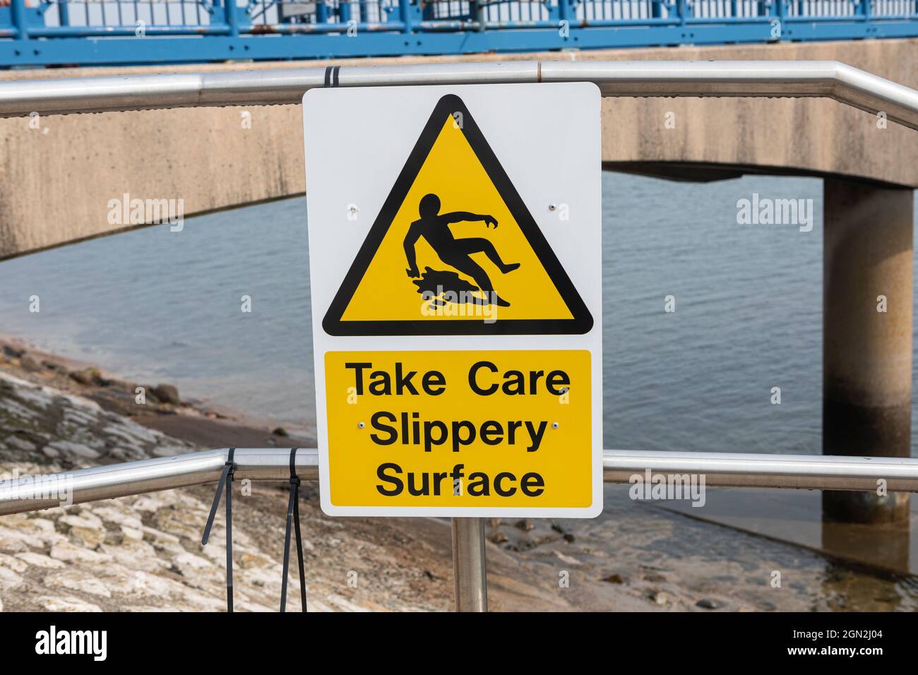 Auf einem kleinen Pier befindet sich ein Warnschild mit „Take Care“ und rutschigem Untergrund. Stockfoto