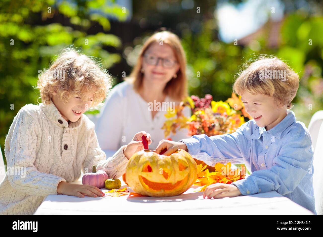 Familie Schnitzerei Kürbis für Halloween-Feier. Eltern und Kinder schneiden Jack o Laterne für traditionelle Trick or Treat Dekoration im sonnigen Garten. Stockfoto