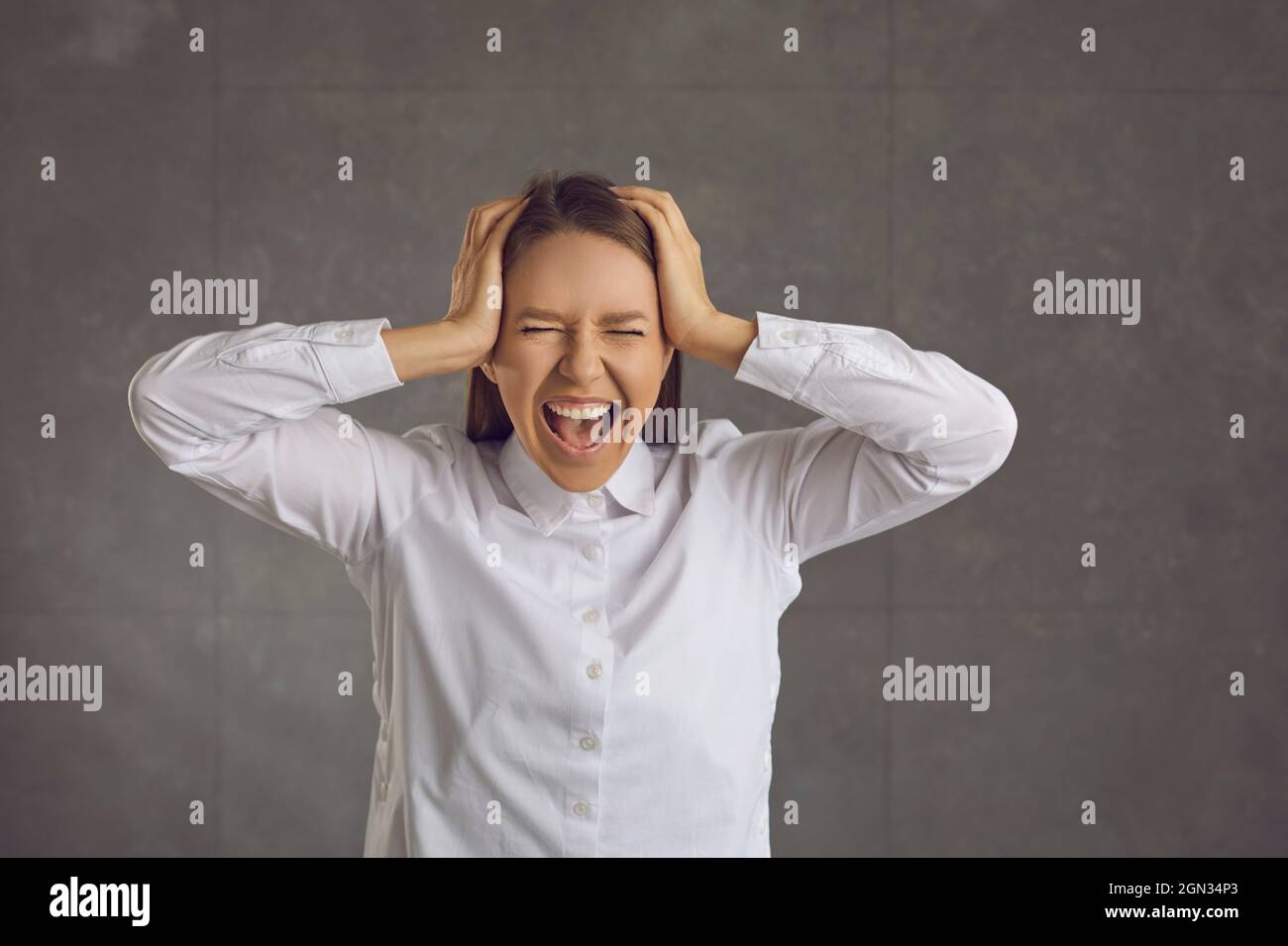 Unglücklich depressive Frau steht auf einem grauen Hintergrund und schreit mit dem Kopf. Stockfoto