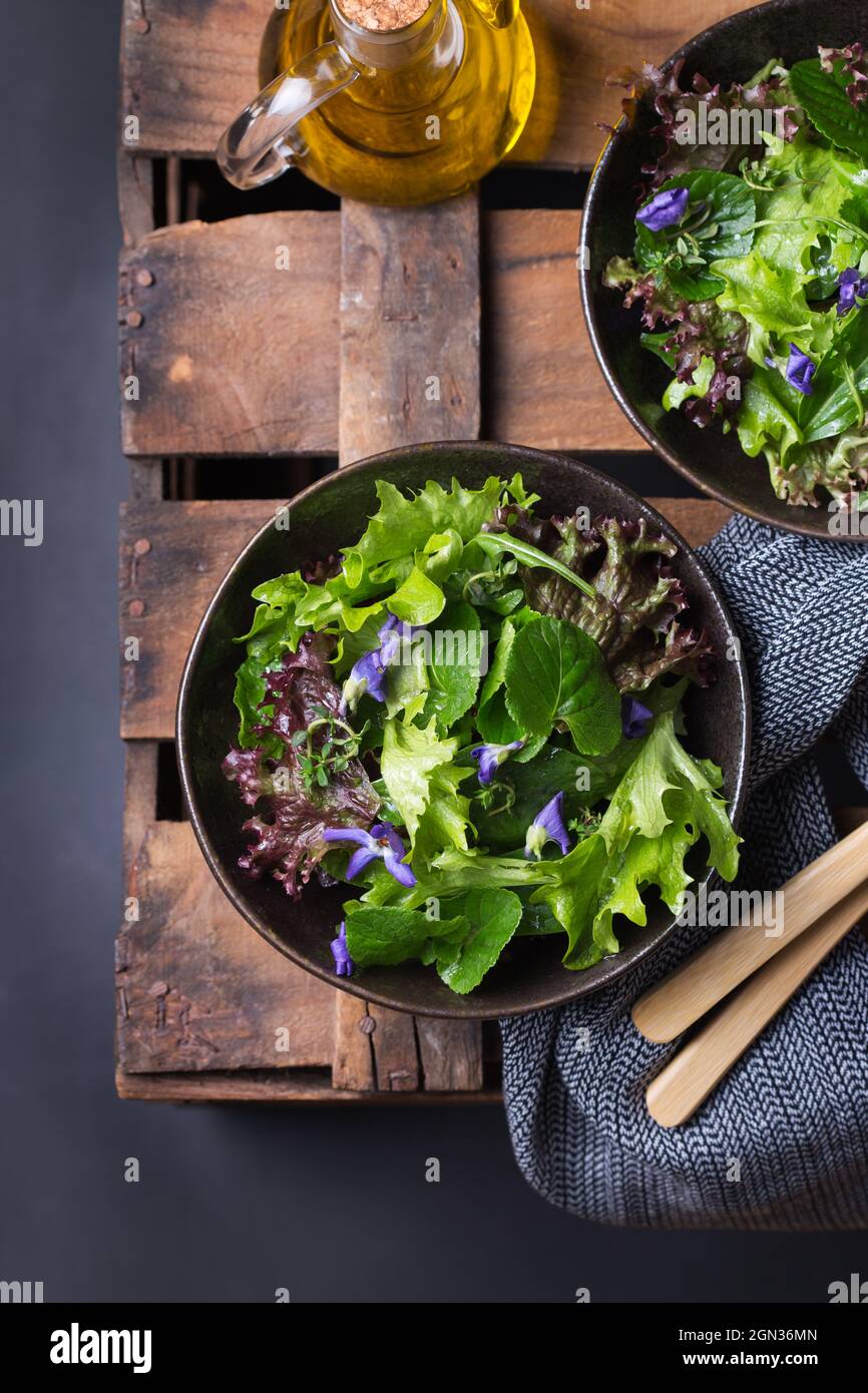 Von oben von leckeren vegetarischen Salat mit grünen und roten Salatblättern und essbaren Blumen gegen Krug Öl Stockfoto