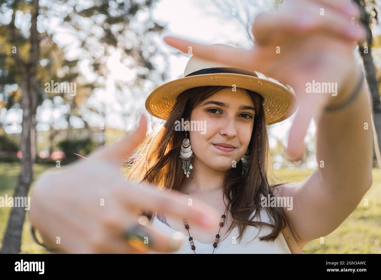 Lächelnde Teenagerin mit Zahnspangen, die eine Geste der Fotografie demonstrieren, während sie tagsüber auf unscharfen Hintergrund die Kamera anschaut Stockfoto