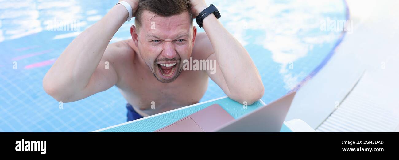 Mann schwimmt im Pool und reißt sich die Haare vor dem Laptop-Bildschirm Stockfoto