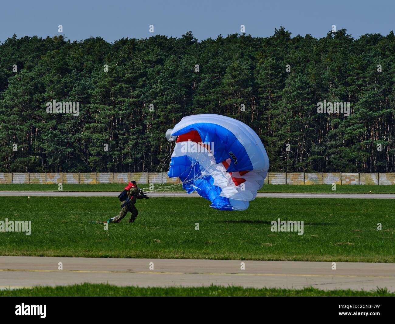 Fallschirmspringer landet auf einer Graspiste, während ein blaues, weißes und rotes Baldachin während einer Flugschau zusammenbricht. Stockfoto