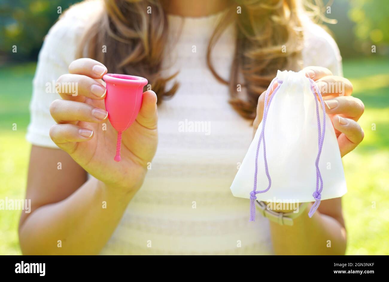 Junge Frau hält eine Menstruationstasse mit Beutel, der vor grünem, natürlichem Hintergrund steht Stockfoto