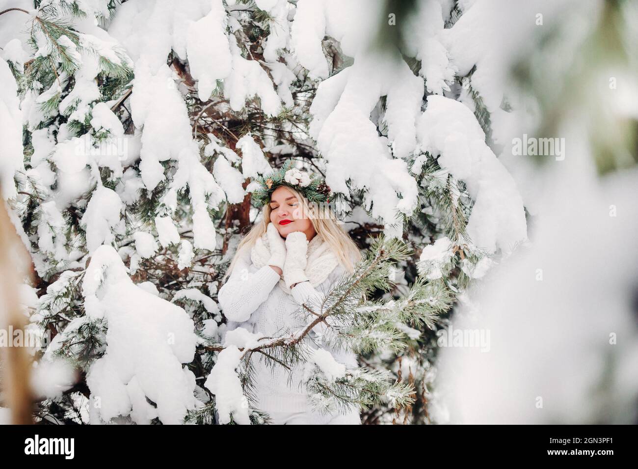 Porträt einer Frau in weißen Kleidern in einem kalten Winterwald. Mädchen mit einem Kranz auf dem Kopf in einem schneebedeckten Winterwald Stockfoto