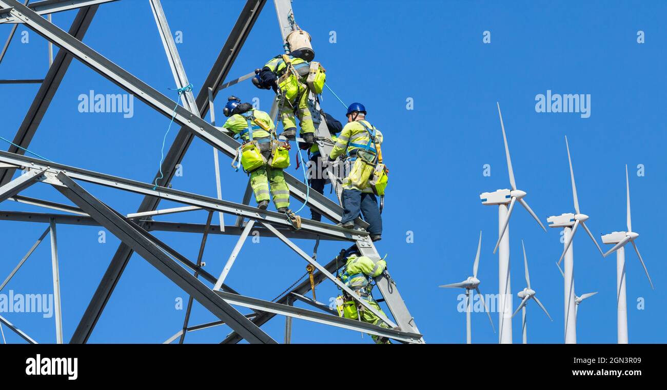 Zusammengesetztes Bild von Ingenieuren von National Grid, die in Großbritannien einen Strompylon mit Windturbinen im Hintergrund bauen. Erneuerbare Energien, Energiepreise... Stockfoto