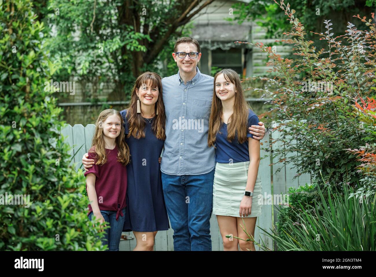 Eine Familie mit Mutter und Vater und zwei Töchtern, die im Sommer oder Herbst auf der hinteren Terrasse eines Hauses draußen stehen Stockfoto