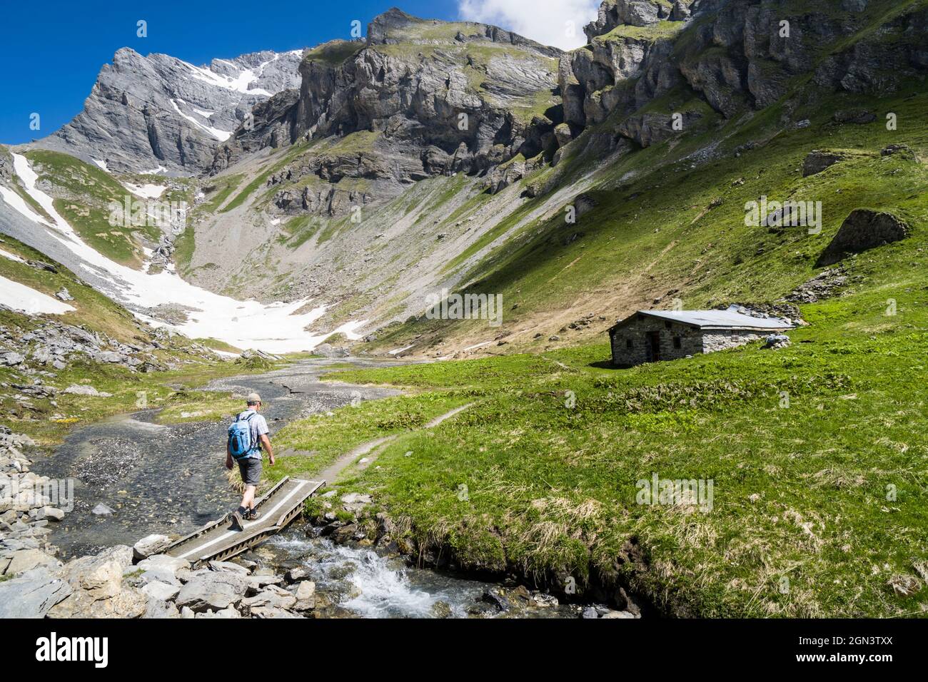 Ein einzelner Wanderer überquert einen Bach, ein alpines Gebäude in den Bergen oberhalb von Ovronnaz, Wallis, Schweiz Stockfoto