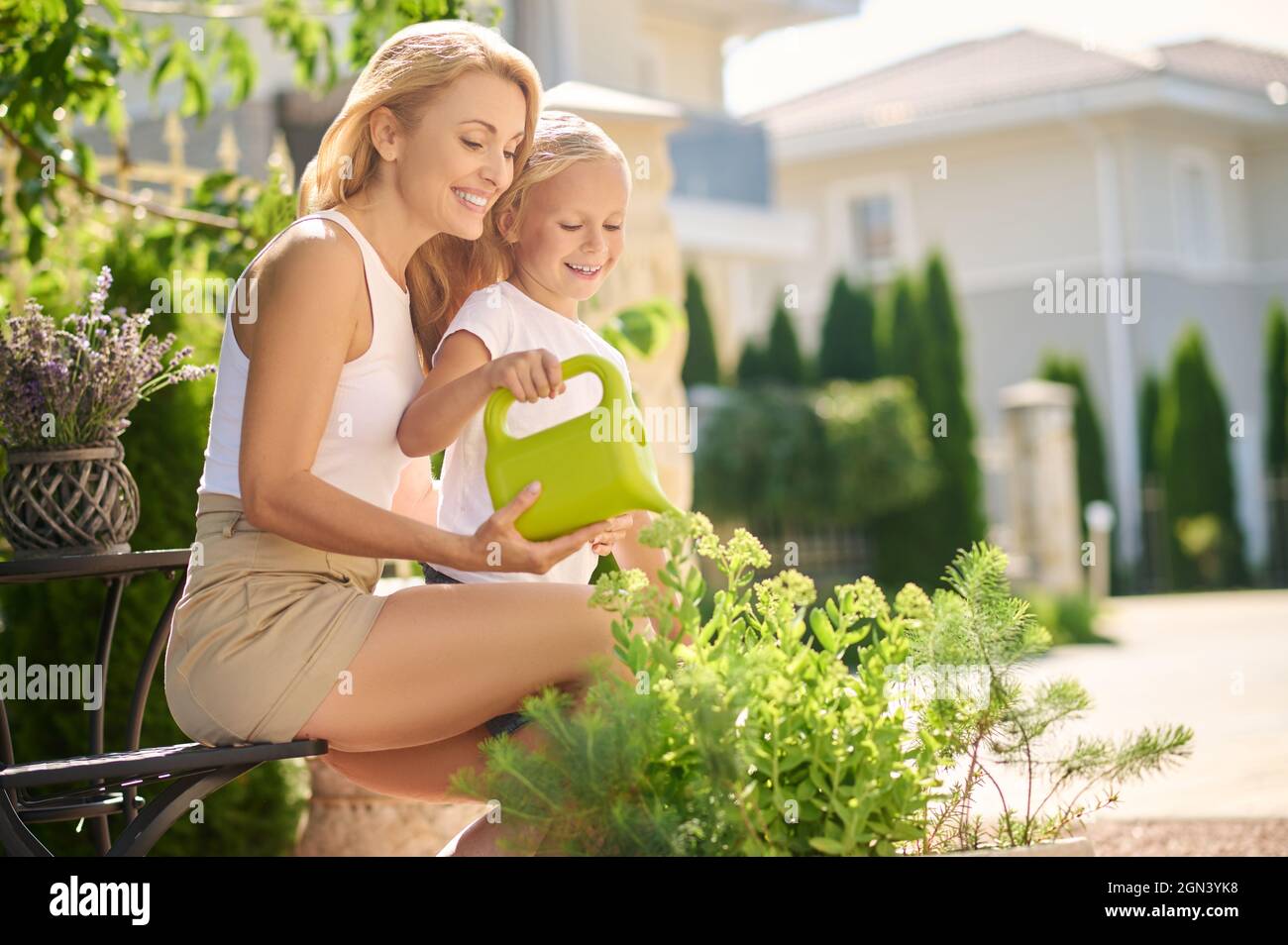 Mutter mit kleiner Tochter, die Blumen in der Nähe des Hauses wässert Stockfoto