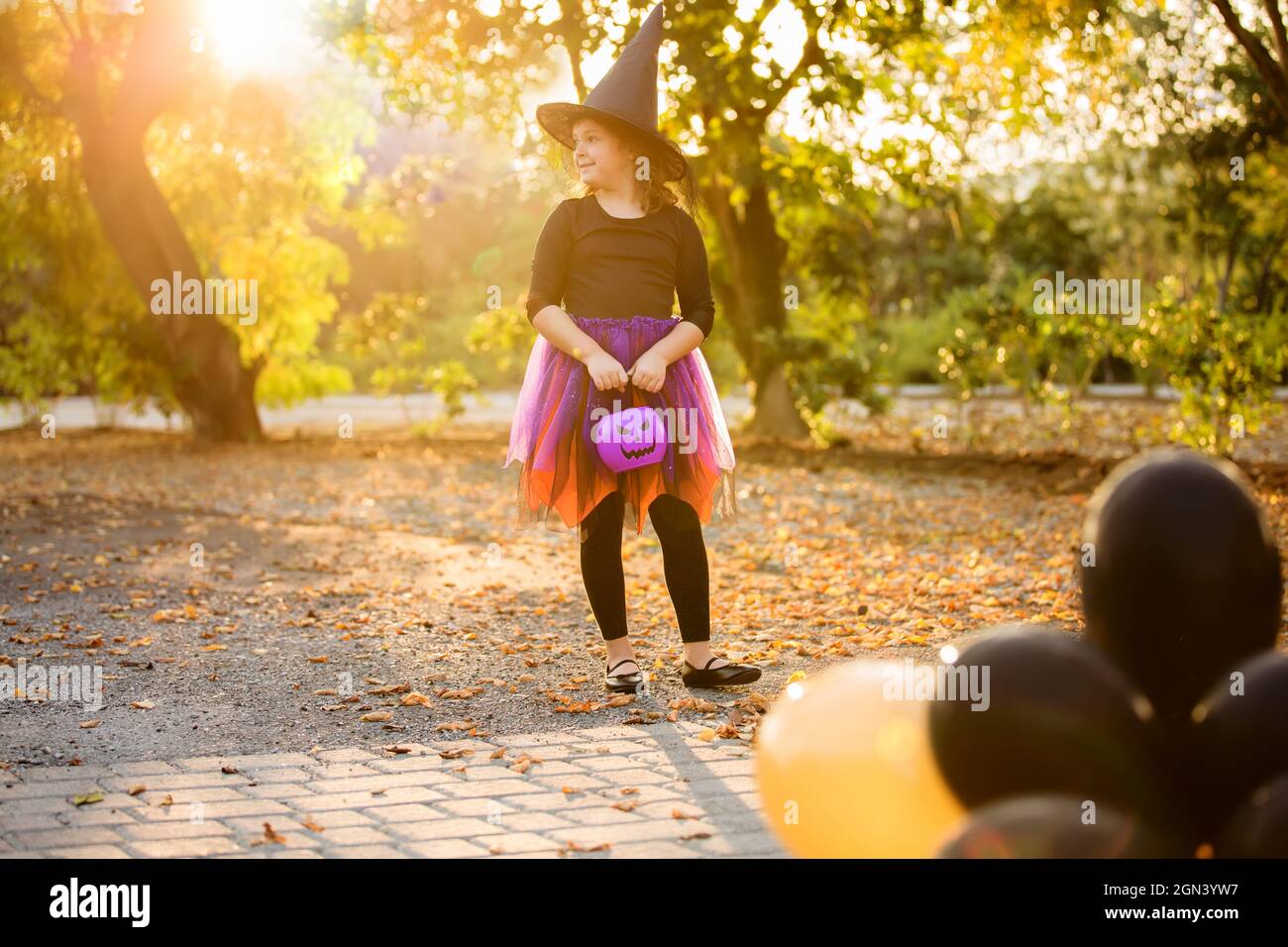 Happy Little Girl feiert Halloween im Freien. Kind im Hexenkostüm und Hut mit orangen und schwarzen Luftballons im Herbstpark.Kindertricks oder Stockfoto