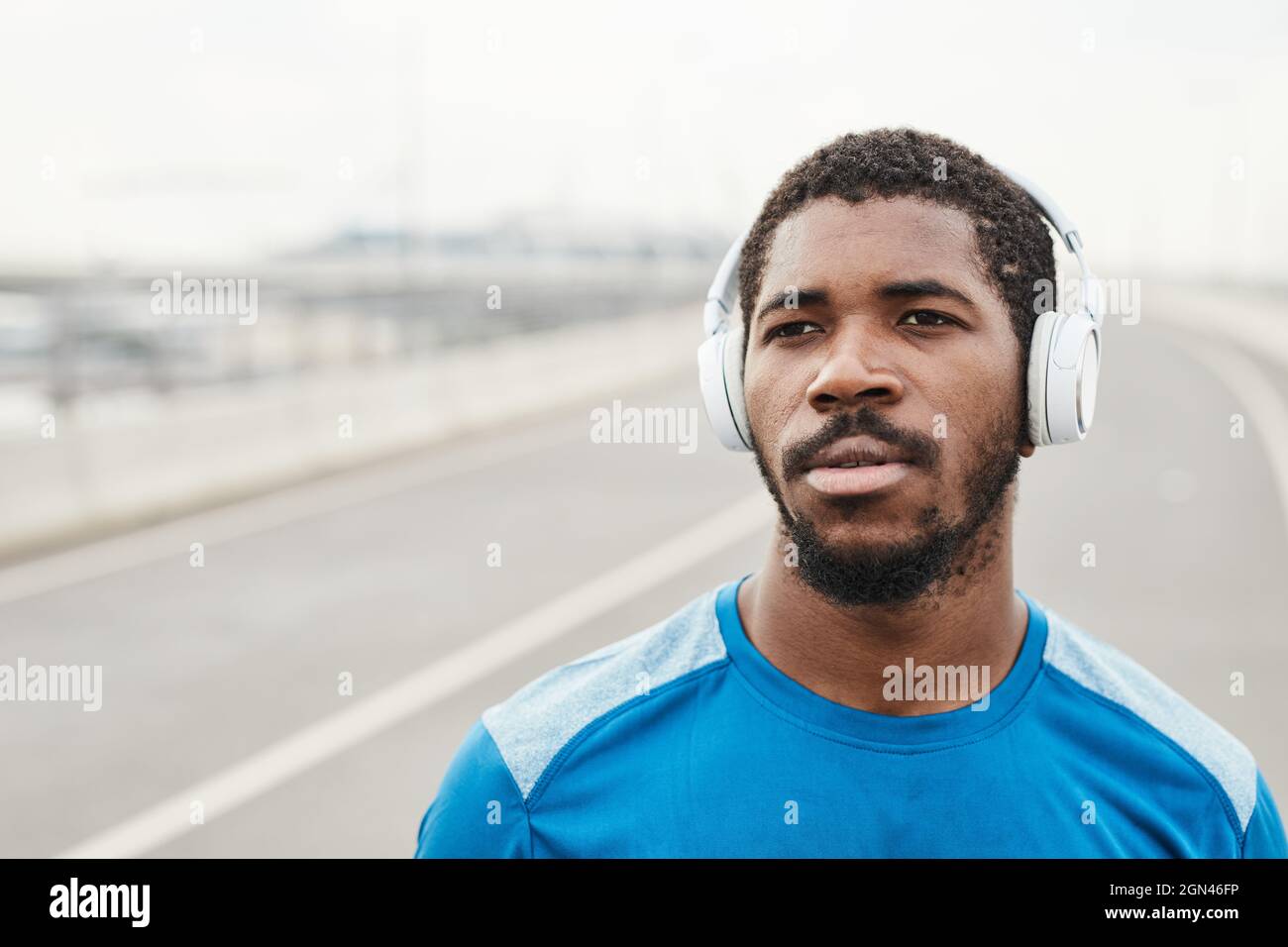 Afrikanischer junger Mann, der kabellose Kopfhörer aufsetzt und beim Laufen im Freien Musik hört Stockfoto