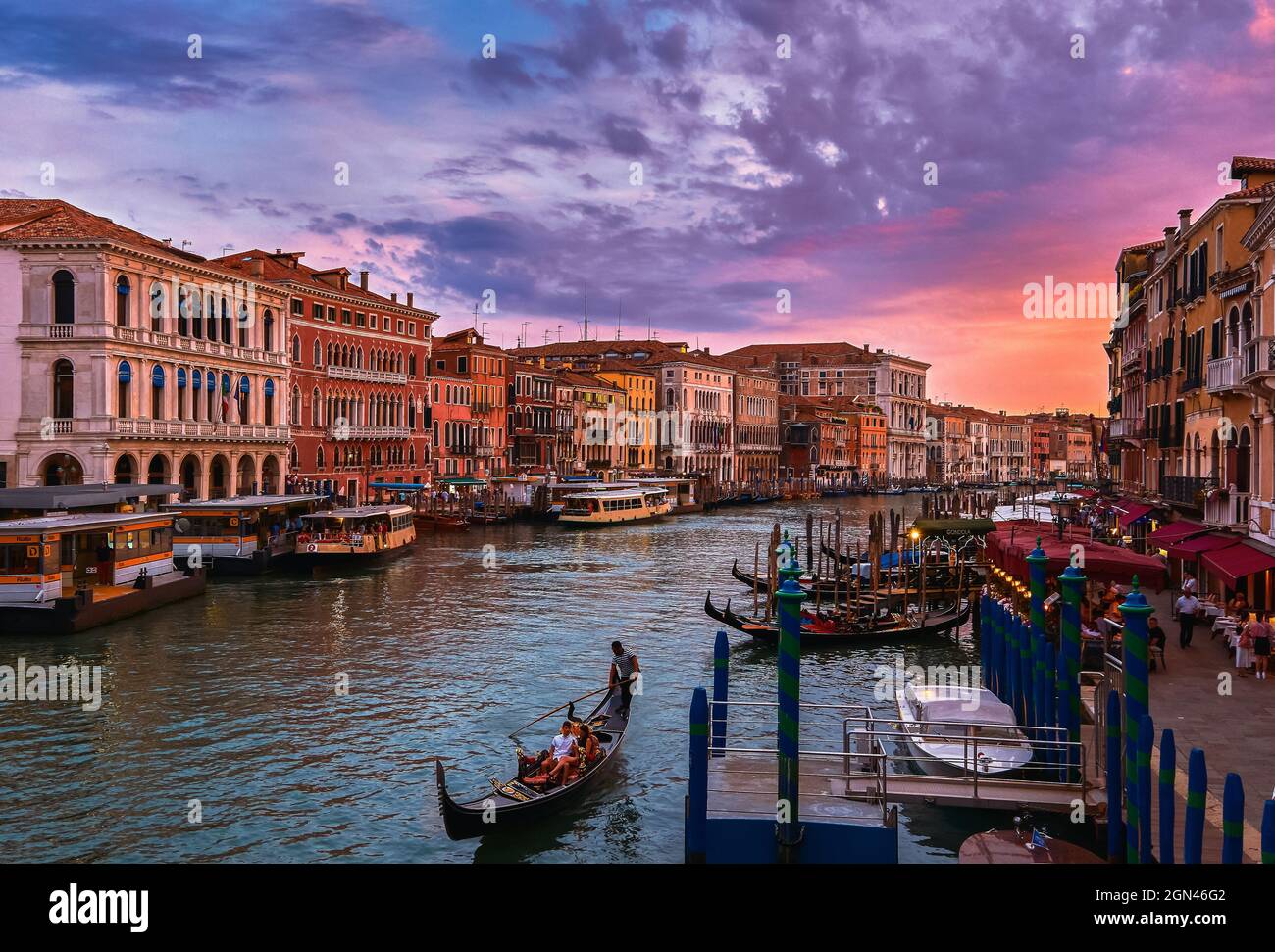 Blick auf den Canale Grande bei Sonnenuntergang, Venedig, Italien. Vaporetto- oder Wasserbus-Station, Boote, Gondeln, die auf Gehwegen festgemacht sind, wunderschöne Sonnenuntergangswolken, UNESCO-Weltkulturerbe Stockfoto