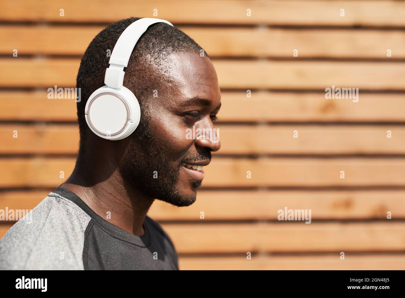 Fröhlicher afrikanischer Sportler, der die Musik in kabellosen Kopfhörern genießt, während er im Freien trainiert Stockfoto